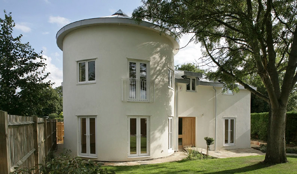 A two storey house with a large round wing to one side, clad with white render